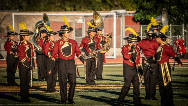 Marching musicians in crimson uniforms and gold plumes on the field at the Wilson Field Tournament on October 24, 2026