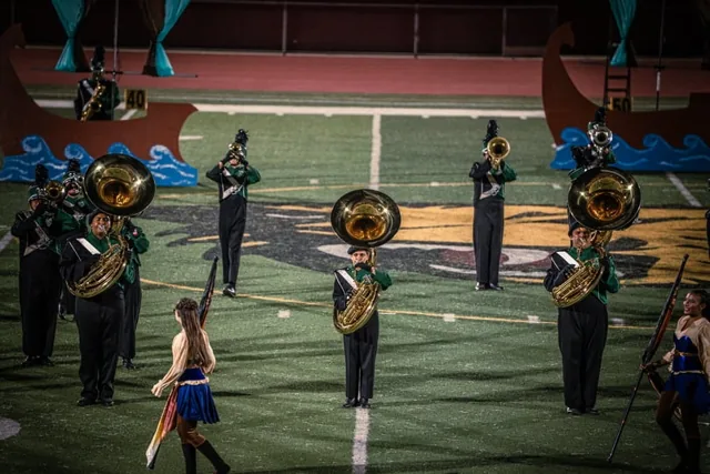 Brass musicians with gold sousaphones performing beside the color guard at the Wilson Field Tournament on October 24, 2026