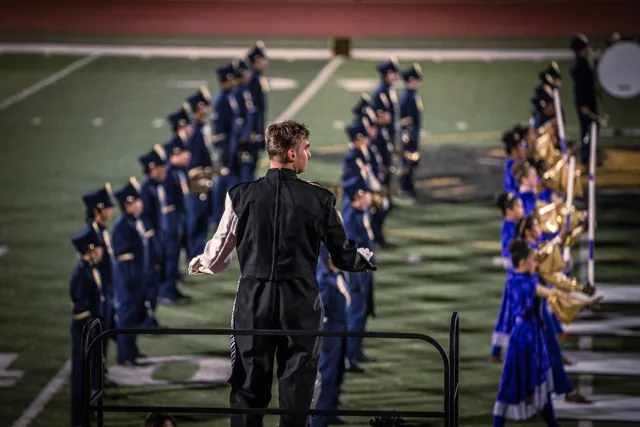 A conductor leading musicians in navy uniforms from a podium at the Wilson Field Tournament on October 24, 2026