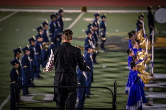 A conductor facing a marching ensemble with blue-clad color guard performers at the Wilson Field Tournament on October 24, 2026